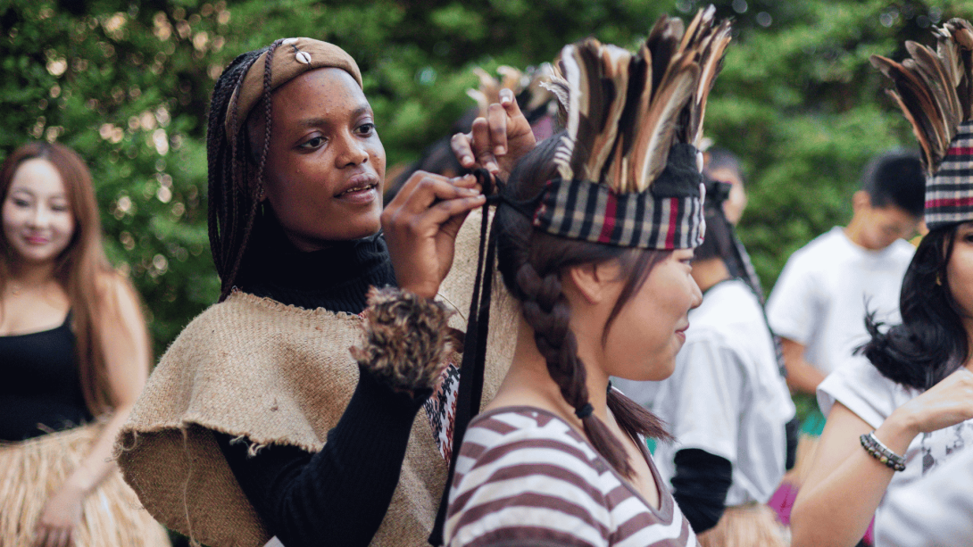 Local woman helps Japanese participant try traditional clothing in Tanzania